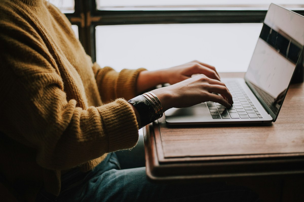 An adult on a laptop at a cafe window